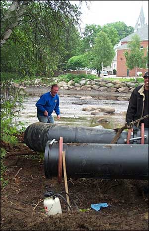 two men smiling while moving large pipes