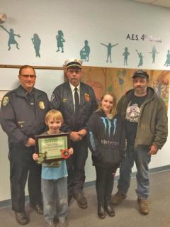 child receiving a 911 award with Police Chief Lester & Fire Chief Gale