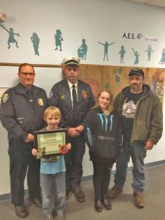 child receiving a 911 award with Police Chief Lester & Fire Chief Gale